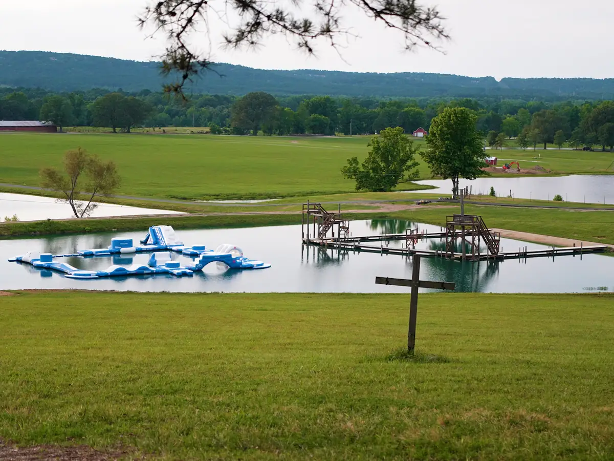 A view of Brookhill Ranch lake with the water inflatable course and a wooden cross in the field